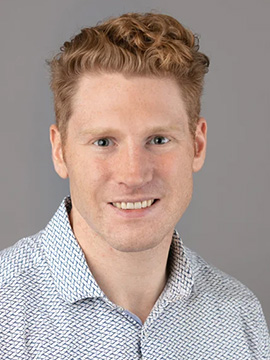 A man with in a collard shirt, smiling at the camera