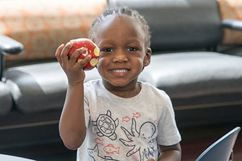 A child holding an apple, smiling.