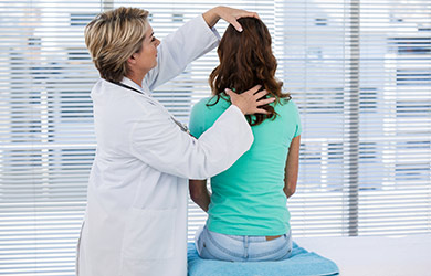 A female physician examining the head and back of a female.