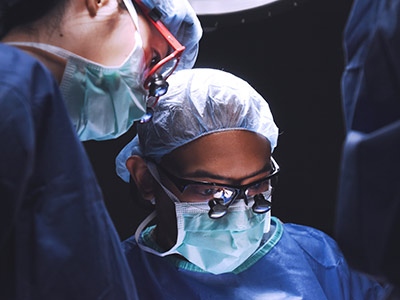 Two surgeons wearing sugical caps, masks and goggles performing surgery.