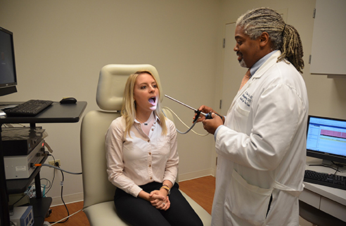 A physician with a tool and a patient with their mouth open.